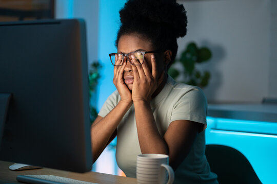 Symptoms Of Overworking. Young Tired Overworked African Woman Freelancer In Eyeglasses Working Late From Home, Sitting In Front Of Monitor, Feeling Eye Strain And Fatigue During Computer Work. 