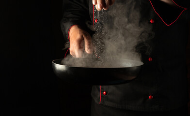 Professional chef adds salt to a hot pan with meat burger cutlets. Free space for hotel menu or...
