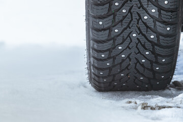 Closeup of black rubber car winter tire with metal studs in cold icey conditions.