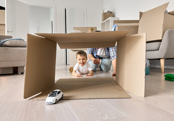 Happy kid son playing toy car with dad unpacking boxes on moving day. Cute small child boy having...