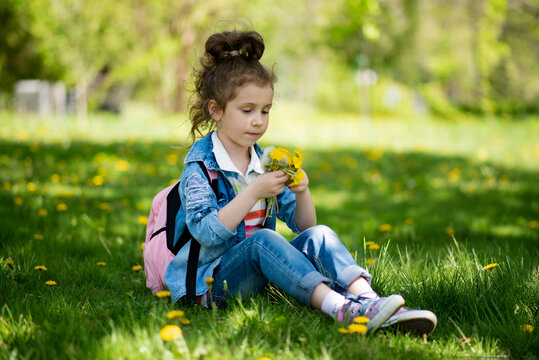 A sweet girl of five years on a walk. It's spring outside and the sun is bright. A girl holds a dandelion in her hands. She is wearing a colored T-shirt and a denim shirt. Childhood. Family.