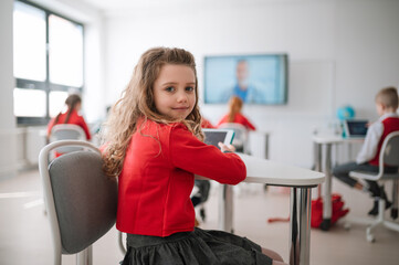 Happy schoolgirl wearing school uniform sitting in class and smiling in the camera.