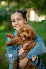 A cute teen girl on a walk with toy poodle dog. It's spring outside. The girl is dressed in a blue jacket in a flower and jeans. Childhood. Pets.