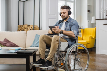 Handsome caucasian man in wheelchair wearing headphones and listening favorite songs while...