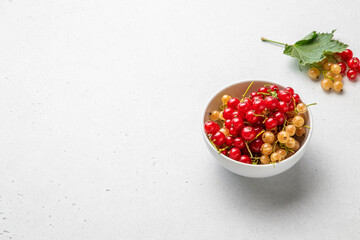 Currant berries with green leaves in white bowl on light background. Red and white currants. Selective focus.