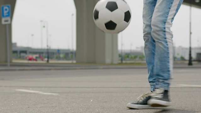 Close-up of man's legs with juggling soccer ball on blurry background. Man is football freestyler kicking soccer ball, guy is juggling ball on street during day.