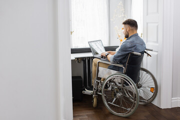 Confident bearded man who using wheelchair typing on wireless laptop at home. Disabled freelancer...