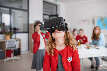 Happy schoolgirl wearing virtual reality goggles at school in computer science class
