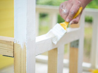 a man's hand with a brush paints a wooden beam with white paint