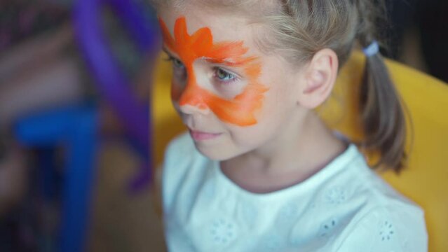 Children face painting. Artist painting with brash and special body paint tiger mask on face of little girl on carnival party for children. Body art painting for childrens.