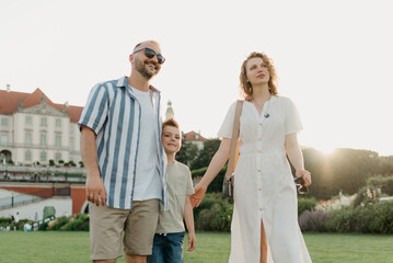 Father, mother and son are hugging in the garden of a European town. Happy family in the evening. Dad is laughing with his family in the background of the palace at sunset.