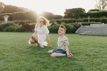 Mother and son are having fun in the garden of an old European town. Happy family in the evening. A boy is showing somersaults to his parent at sunset.