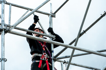 An industrial climber wearing a helmet and a protective belt is tied with a rope to a support at a...