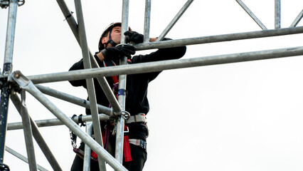 An industrial climber wearing a helmet and a protective belt is tied with a rope to a support at a...
