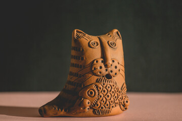 Clay figurine of a cat with a fish on a dark background close-up. Crafts made of clay. A cat holds a fish in its paws. Chocolate figurines. Chocolate dessert close-up.