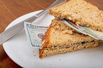 'Consumer staples inflation concept of US 100 dollar bill sandwich with whole grain bread slices on dinner plate.'