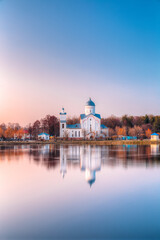 Alexander Nevsky Orthodox Christian Church With Bell Tower And Chapel On Lake Shore In Sunset Sunrise Dawn, Early Spring, Forest Park Background. Gomel, Homiel, Belarus