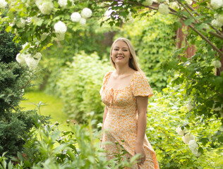 Young Slavic blonde girl with long hair on the background of blooming viburnum Boule de Neige