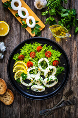 Fried calamari rings with lemon, greens and cherry tomatoes on wooden table 