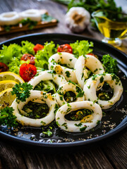 Fried calamari rings with lemon, greens and cherry tomatoes on wooden table 