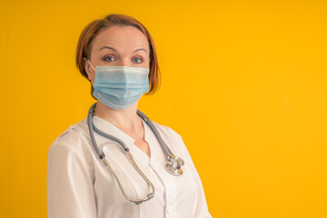 portrait of female doctor in medical mask and stethoscope on yellow background with copy space