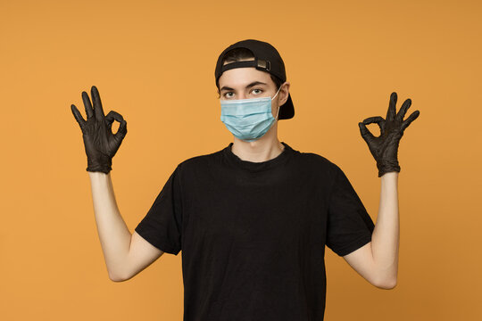 a young man in a black T-shirt, mask and gloves shows an OK sign with two hands, colored background