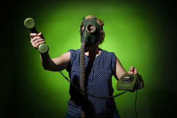 A woman in a gas mask passes the receiver of a retro phone on a dark dramatic background, hard...