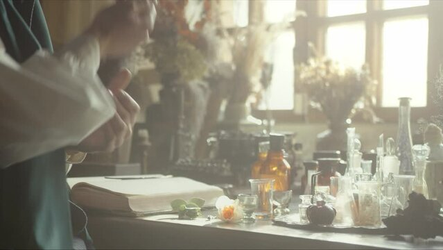 A close-up of a perfumer at his desk looking for a new fragrance. Vintage cinematic concept. Sunny day in the workshop. Lots of ingredients, glass flasks on the table. Concept of perfumery. 4K video