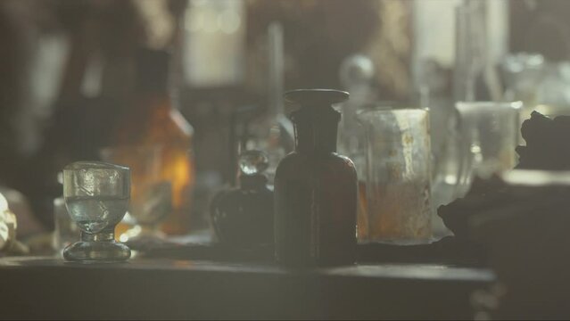 Close-up of a perfumer's workplace. Vintage cinematic concept. Sunny day in the working workshop. Lots of ingredients, a book, glass flasks on the table. Depth of field. 4K video
