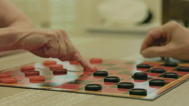 A Caucasian man and woman engaged in a game of checkers on a old fashion checker board.