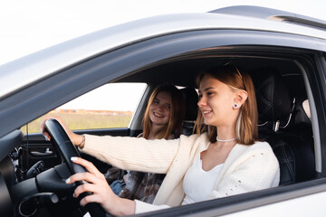 Two young women laughing in the car during a summer road trip. Best friends have fun together as they drive through the countryside. A happy couple of girls relaxing on a road trip.