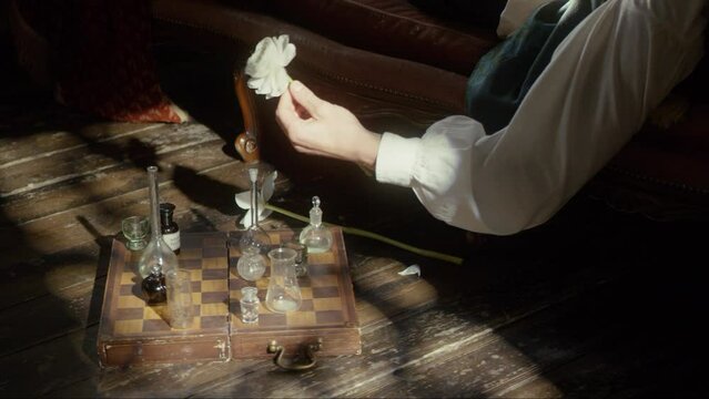 A man's hand holds a white flower, puts it on the floor and plays chess with flasks. The concept of a perfumer, rest, creative crisis, reflection. Cinematic concept. Close-up. 4K video, RED camera