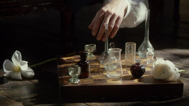 A man's hand plays chess with flasks on a chessboard. The concept of a perfumer, relaxation, creative crisis, reflection, play, invention. Cinematic concept. Close-up. 4K video, RED camera