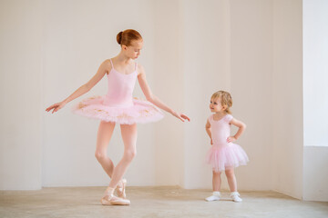 The older sister, a ballerina in a pink tutu and pointe shoes, shows the baby how to practice at...