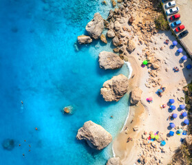 Aerial view of blue sea, beach with umbrellas, rocks in water