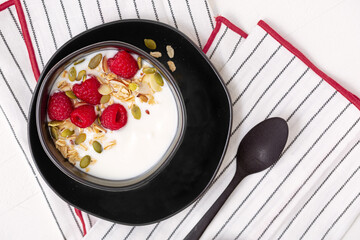 Overhead view of vanilla yogurt with granola and fresh raspberries; copy space