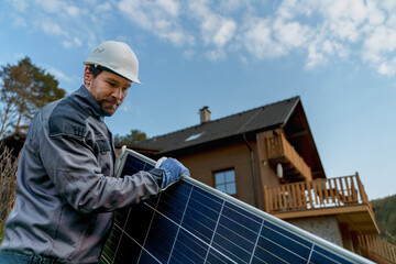 Smiling handyman solar installer carrying solar module while installing solar panel system on house. © Halfpoint