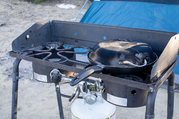 Outdoor camping propane stove with cast iron cooking pots on top with tent in background in Utah...