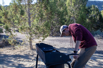 Man in sweatshirt investigating a outdoor propane camping stove to cook food at camp site in Utah...