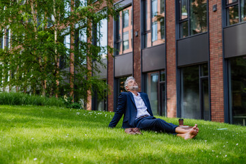 Mature businessman resting and sitting barefoot in park, feeling free, escaping from work, work...
