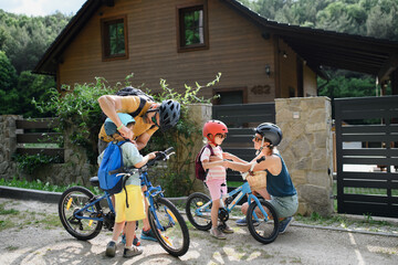 Portrait of young family with little children preapring for bike ride, standing with bicycles in...