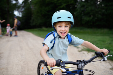 Portrait of excited little boy with his family at backround riding bike on path in park in summer