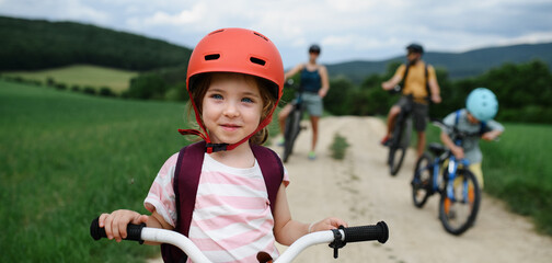 Portrait of excited little girl with his family at backround riding bike on path in park in summer