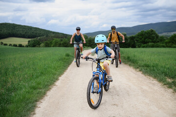Portrait of excited little boy with his parents at backround riding bike on path in park in summer
