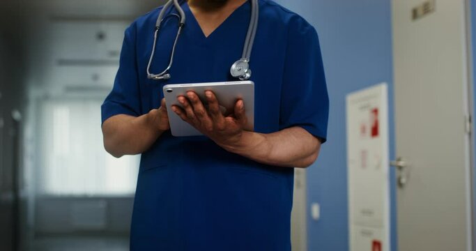 African American doctor uses a tablet standing in corridor of medical center