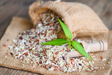 brown rice in the sack with wooden background , raw various rice color mixed thai rice for cooking food , Loonzain rice brown black red white purple health food.