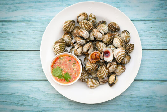 Fresh raw shellfish blood cockle ocean gourmet seafood in the restaurant, Cockles on white plate with seafood sauce on table background - top view