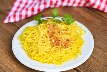 yellow noodles on white plate and wooden background , instant noodles yellow noodles rice vermicelli food with fried garlic and coriander