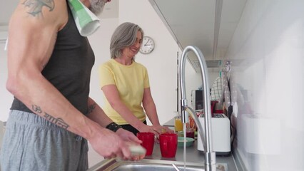 Healthy sporty happy senior adults family couple washing dishes at home. Mid age older man and woman enjoying talking, doing household activity in kitchen in the morning. - Powered by Adobe
