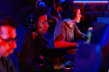 Side view portrait of young black man playing video games with diverse eSports team in neon light